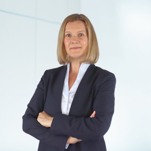 The picture shows a woman with half-length, blonde hair. She is wearing a light blue blouse and a blue blazer. She smiles friendly into the camera.