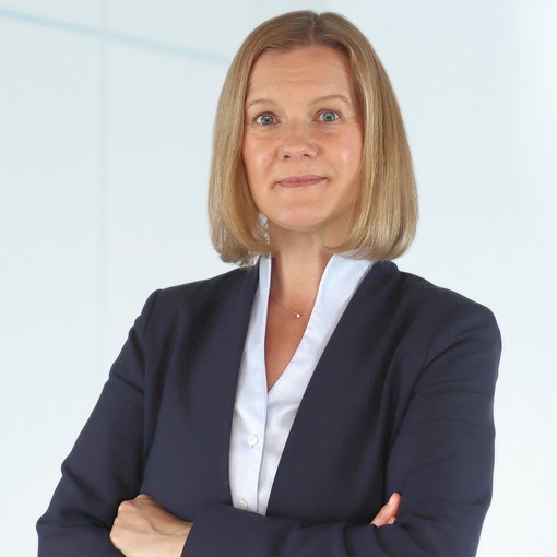 The picture shows a woman with half-length, blonde hair. She is wearing a light blue blouse and a blue blazer. She smiles friendly into the camera.